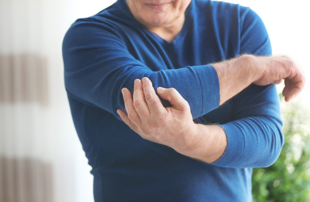 Mature man in blue shirt massaging his sore elbow at home, elbow pain treatment at Mast Health in Tampa
