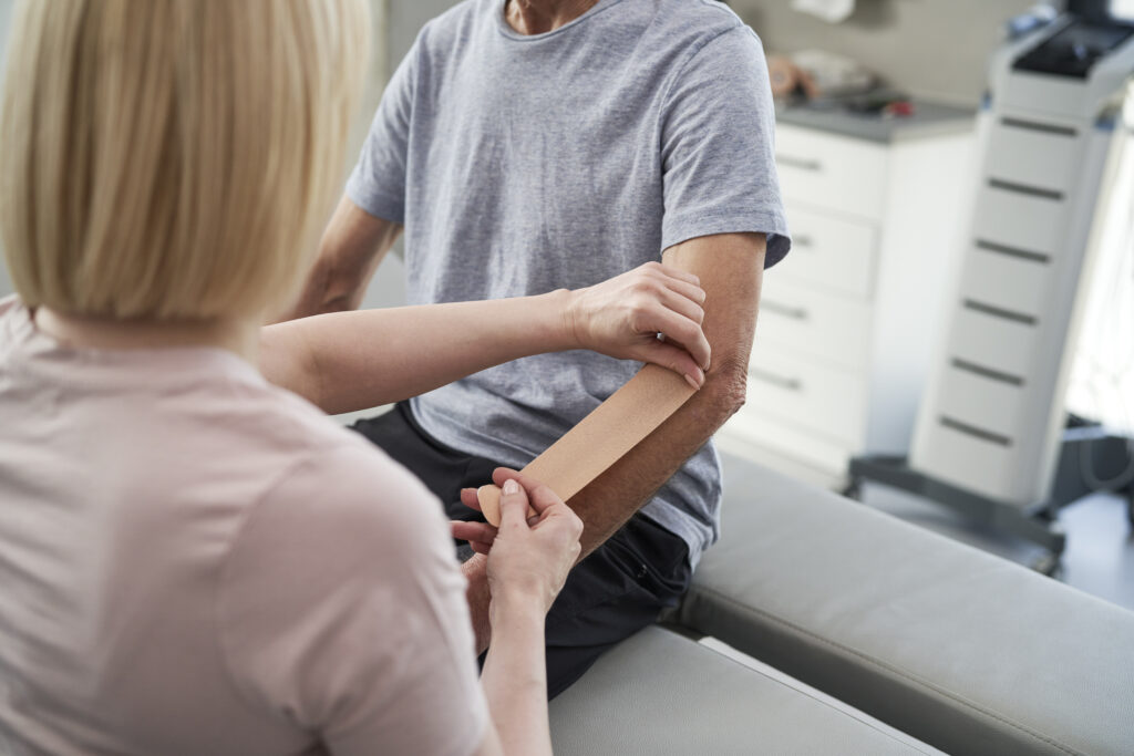 Physical therapist applying kinesiology tape to patient's forearm during rehabilitation, elbow pain therapy at Mast Health in Tampa