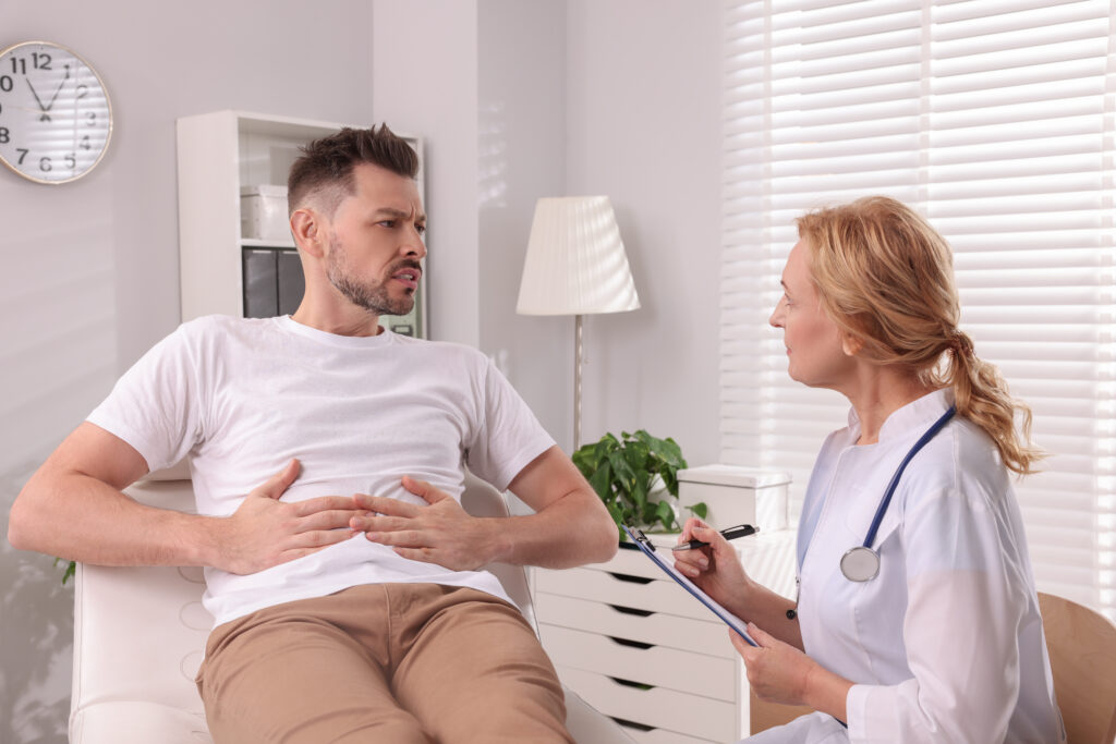 Doctor listening while male patient holds his stomach and describes digestive discomfort during a clinic consultation in Tampa