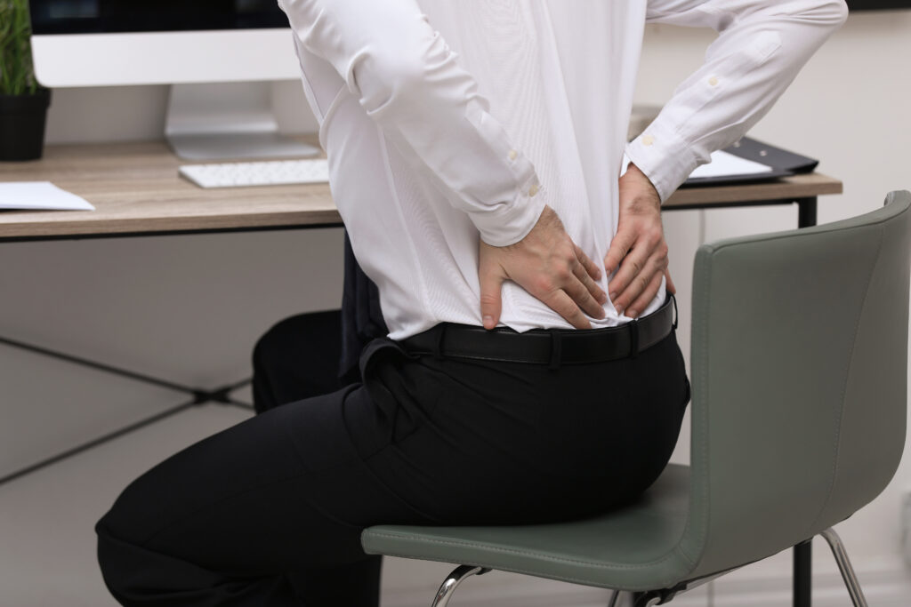 Businessman standing at his office desk holding his lower back in pain, herniated disc relief Mast Health offers Tampa office workers
