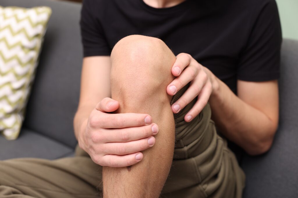 Young man on his sofa suffering from knee pain at home