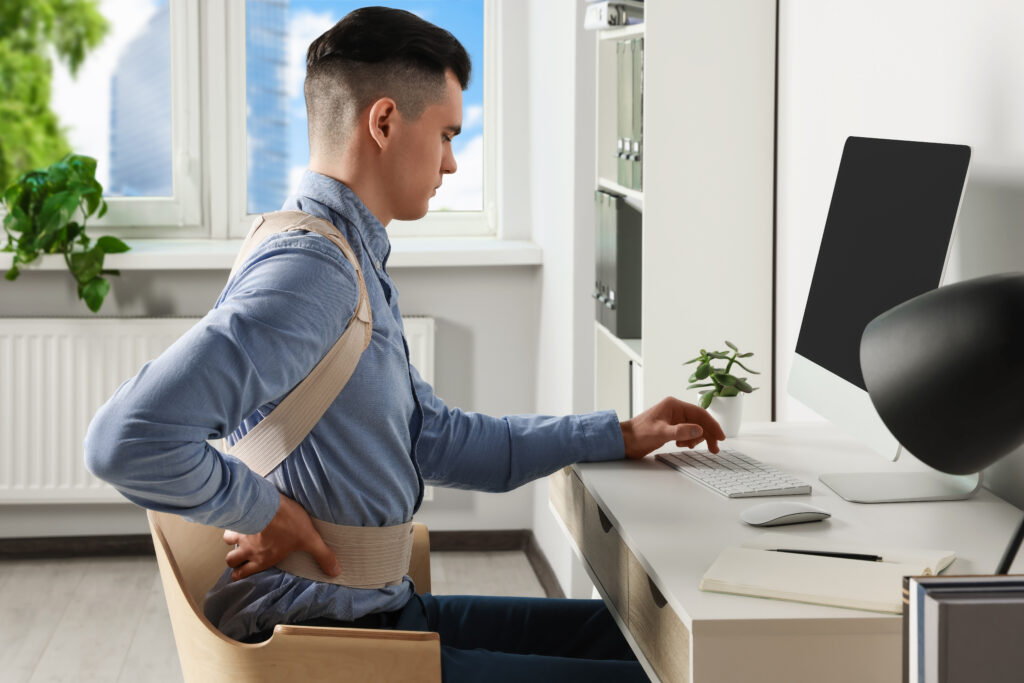 Man wearing an orthopedic back support brace while working at his desk, herniated disc relief Mast Health offers Tampa office workers