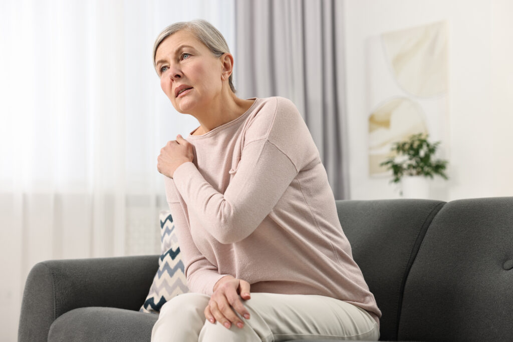 Mature woman sitting on a sofa massaging her sore shoulder, muscle tension relief for fibromyalgia at Mast Health in Tampa