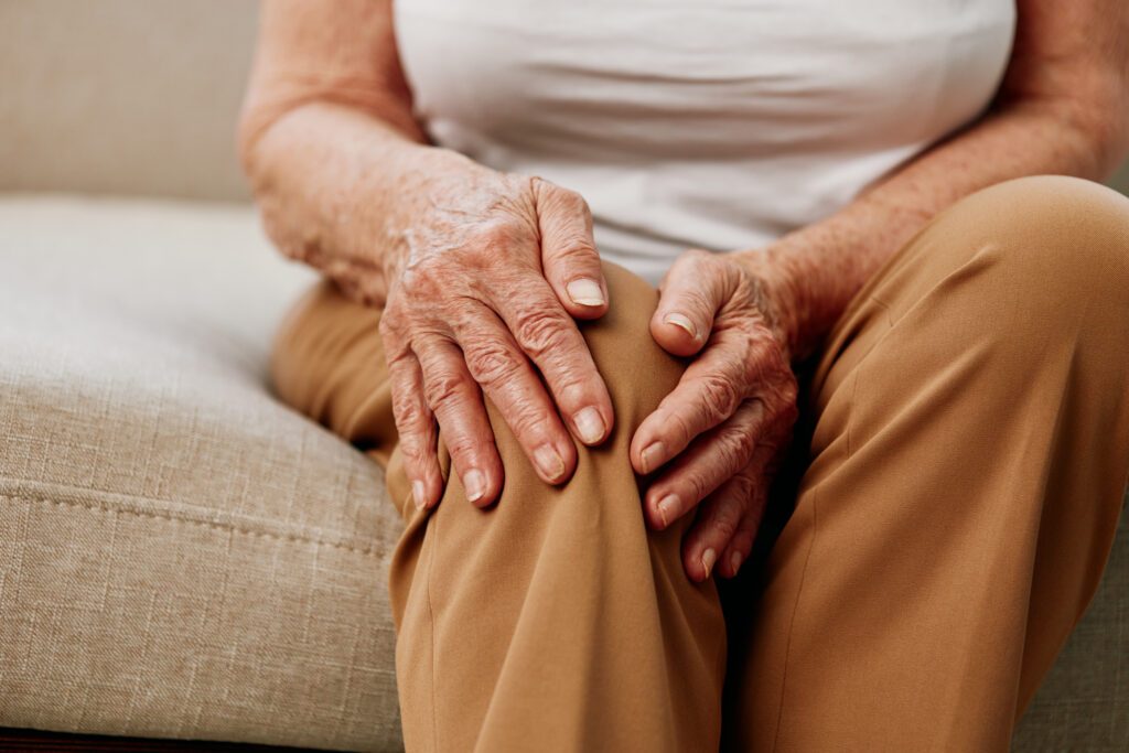 Elderly woman holding her sore knee due to joint and ligament pain