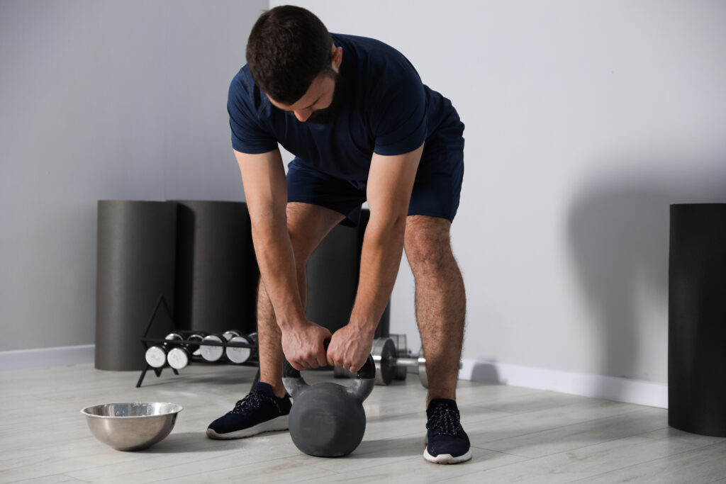 Man bending forward to lift a kettlebell in the gym, exercise related back strain that can lead to a herniated disc Mast Health treats in Tampa