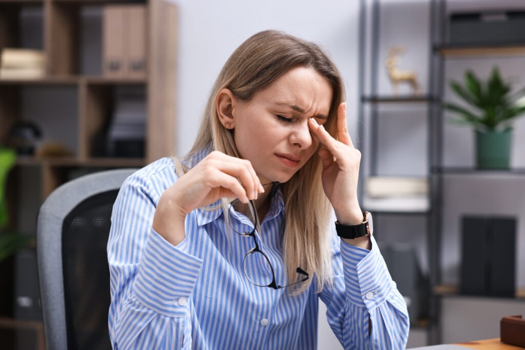 Woman in office attire pressing her fingers to the bridge of her nose in pain, tension headache relief Mast Health offers Tampa professionals