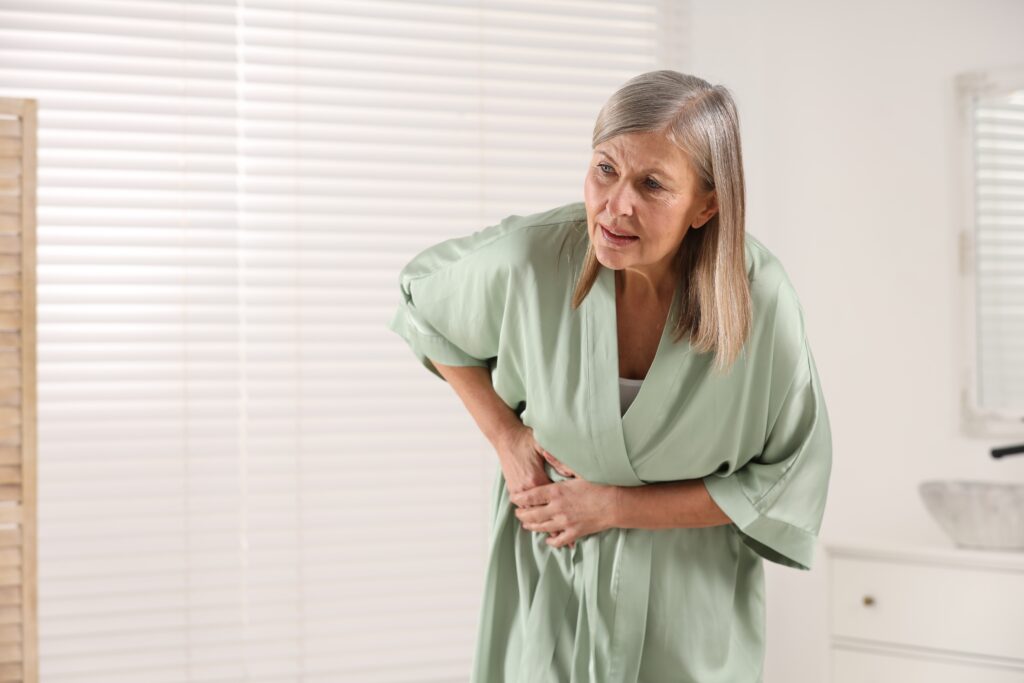 Woman in a robe holding her stomach in pain and discomfort at home, gentle whole body support for fibromyalgia at Mast Health in Tampa