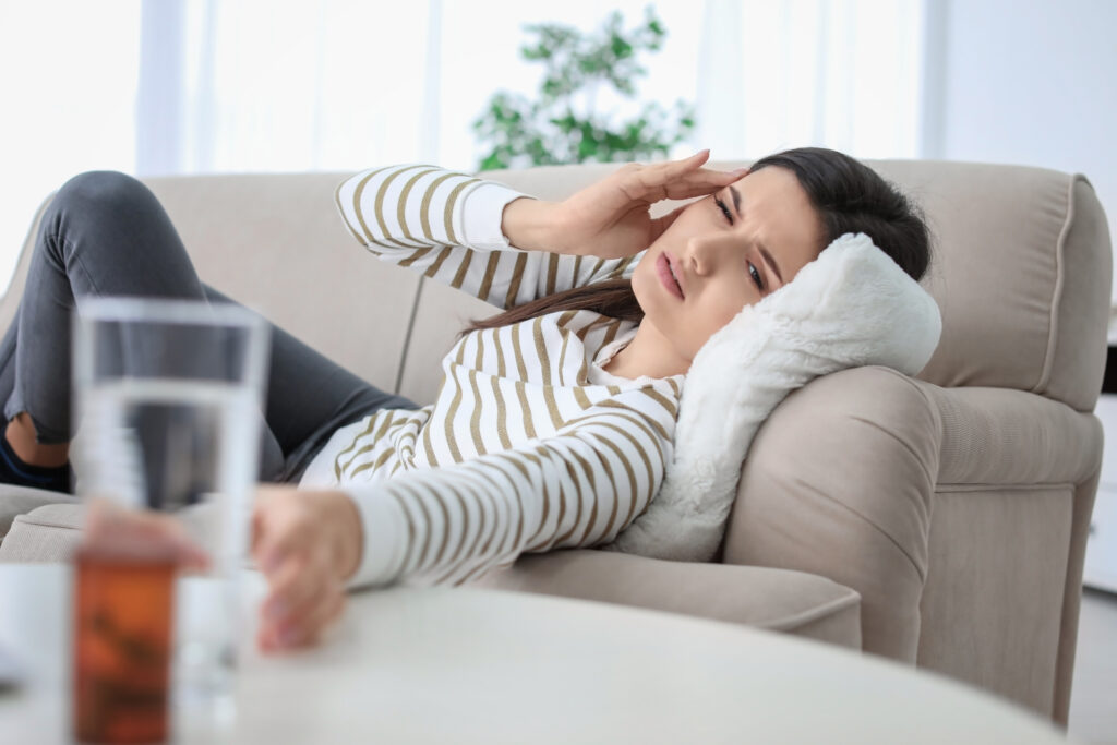 Young woman lying on sofa at home pressing hand to her temple in headache pain, headache and migraine relief at Mast Health in Tampa