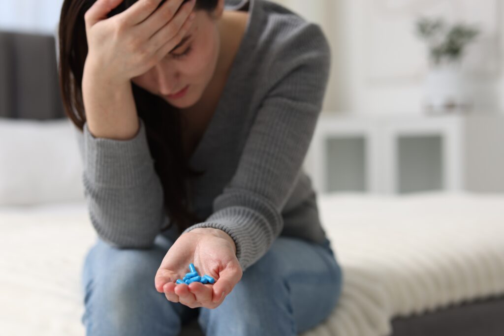Woman holding her head in pain while holding pills in her other hand, relying on pain relievers for recurring headaches Mast Health treats at the source in Tampa