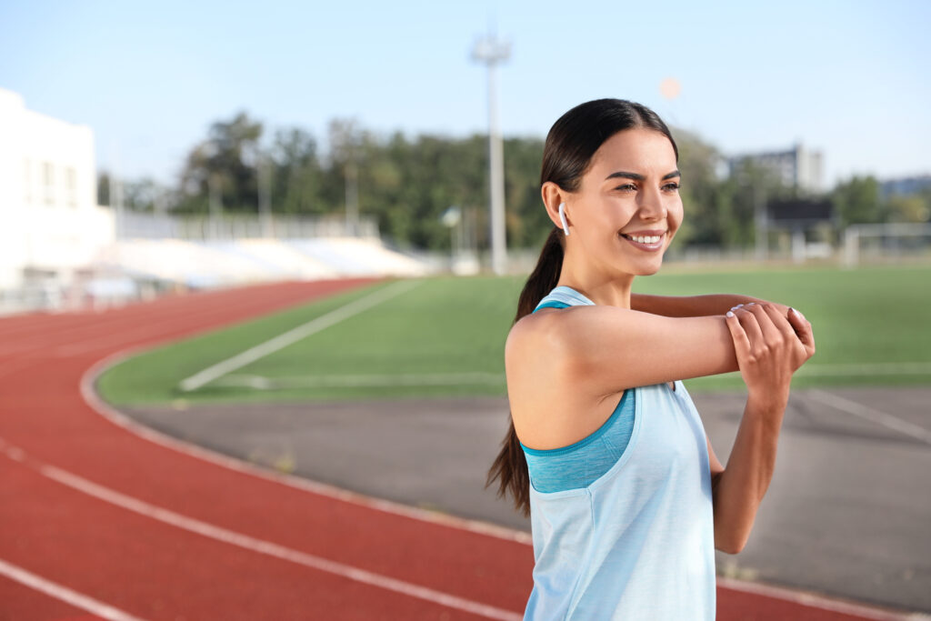 Young sportswoman stretching her arm outdoors at a stadium track, injury prevention for elbow pain at Mast Health in Tampa