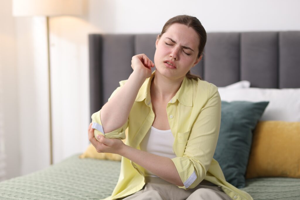 Young woman sitting on a sofa at home wincing while holding her painful elbow, elbow pain treatment at Mast Health in Tampa