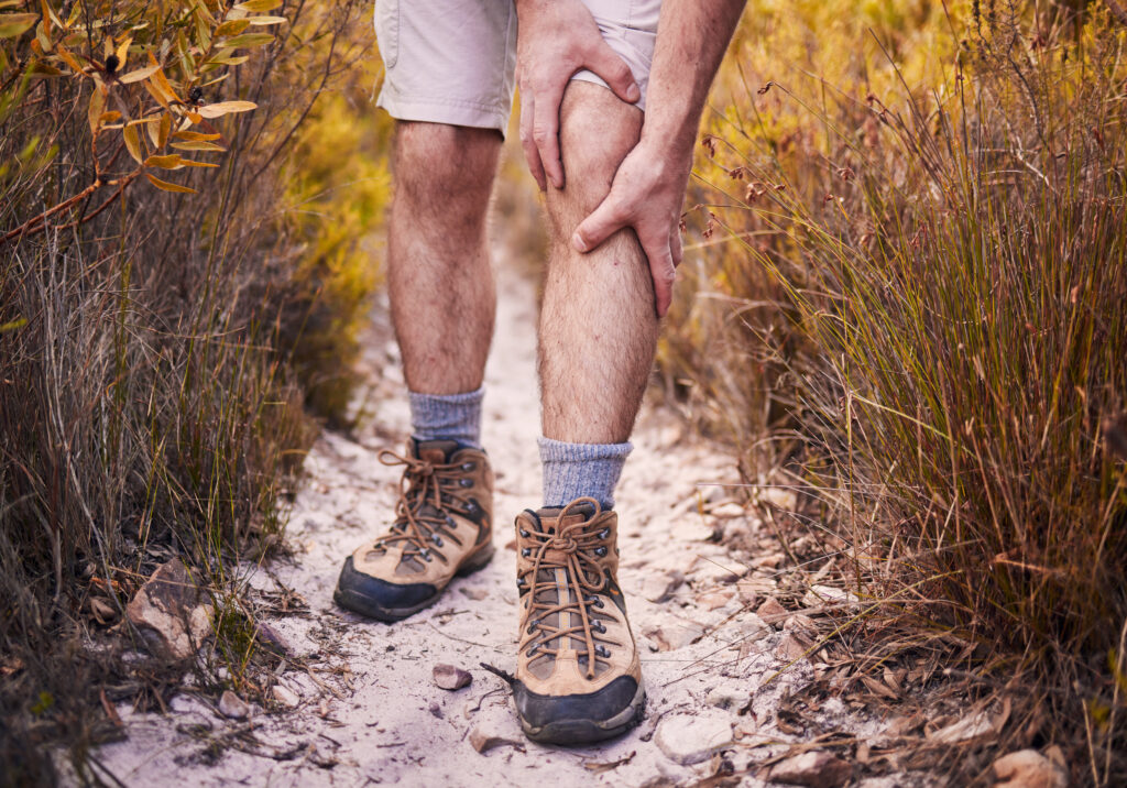Man hiking on a trail and gripping his knee in pain, knee pain Mast Health treats to keep Tampa hikers active