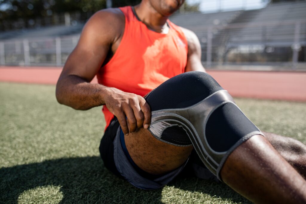 Athlete on a track adjusting a knee brace for support, Mast Health helps Tampa athletes manage overuse injuries