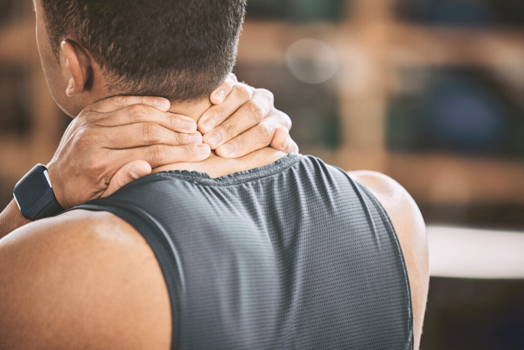 Athletic man gripping the back of his neck in pain during a gym workout, a common trigger for neck strain treated at Mast Health in Tampa, FL