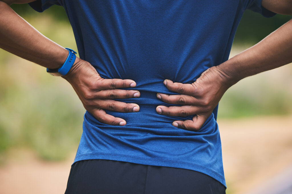 Man in athletic wear holding his lower back in a park after exercise, back pain relief Mast Health provides for active Tampa residents