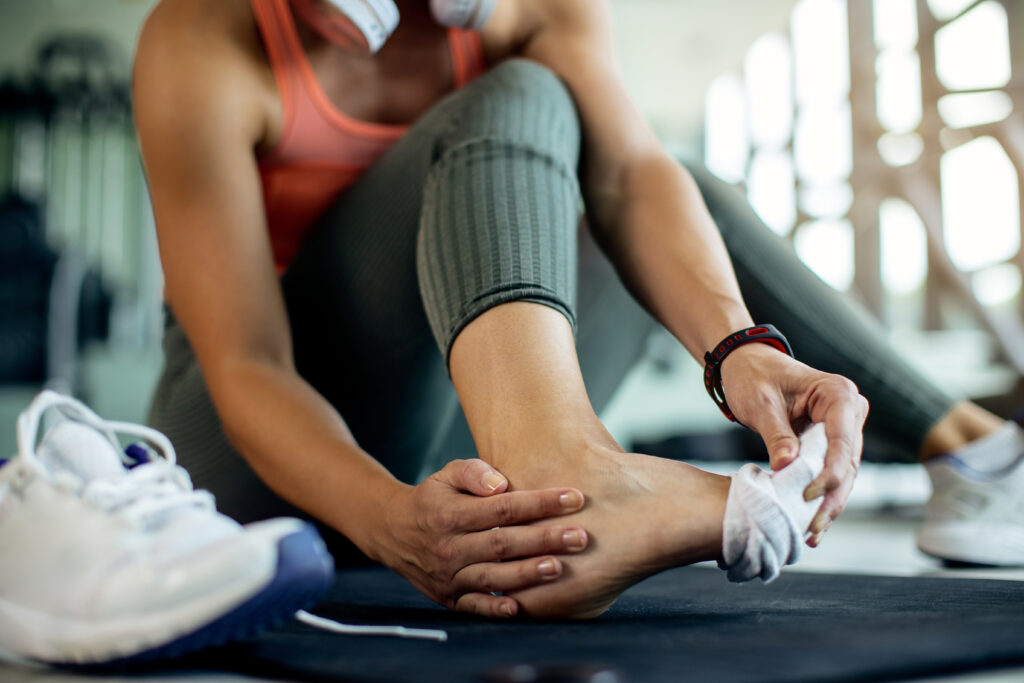 Close-up of a woman holding her ankle in pain at the gym after exercising, a common overuse injury treated at Mast Health in Tampa, FL