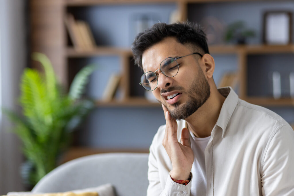 Young man at home holding his cheek in jaw pain, TMJ and facial discomfort relief at Mast Health chiropractic clinic in Tampa, FL