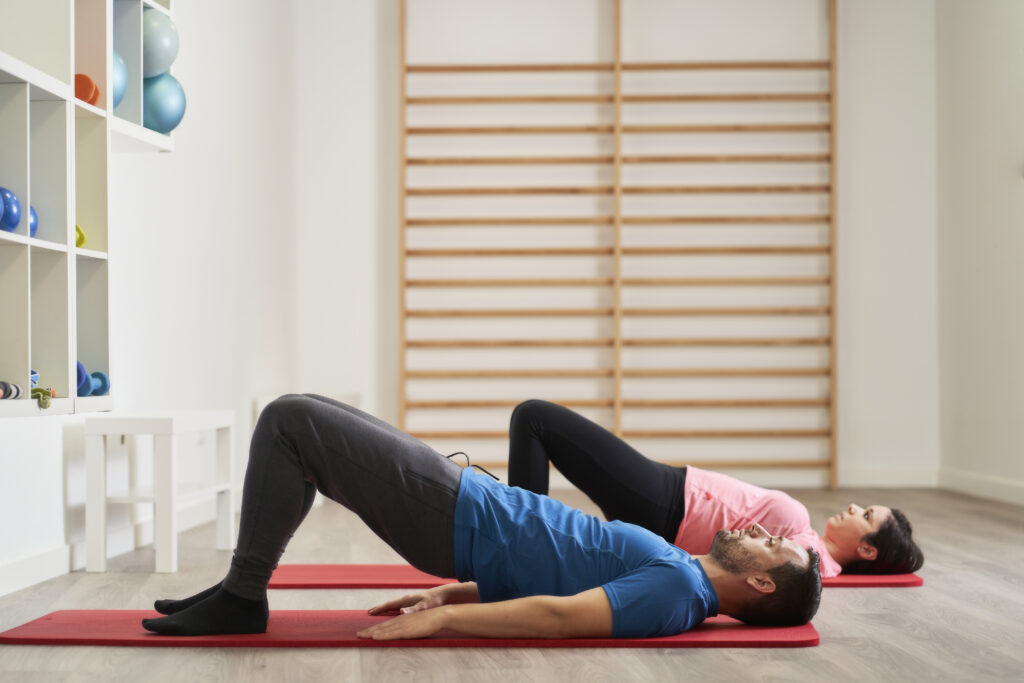 Couple performing a bridge exercise on yoga mats indoors, core and low back exercises supporting sciatica relief at Mast Health in Tampa, FL