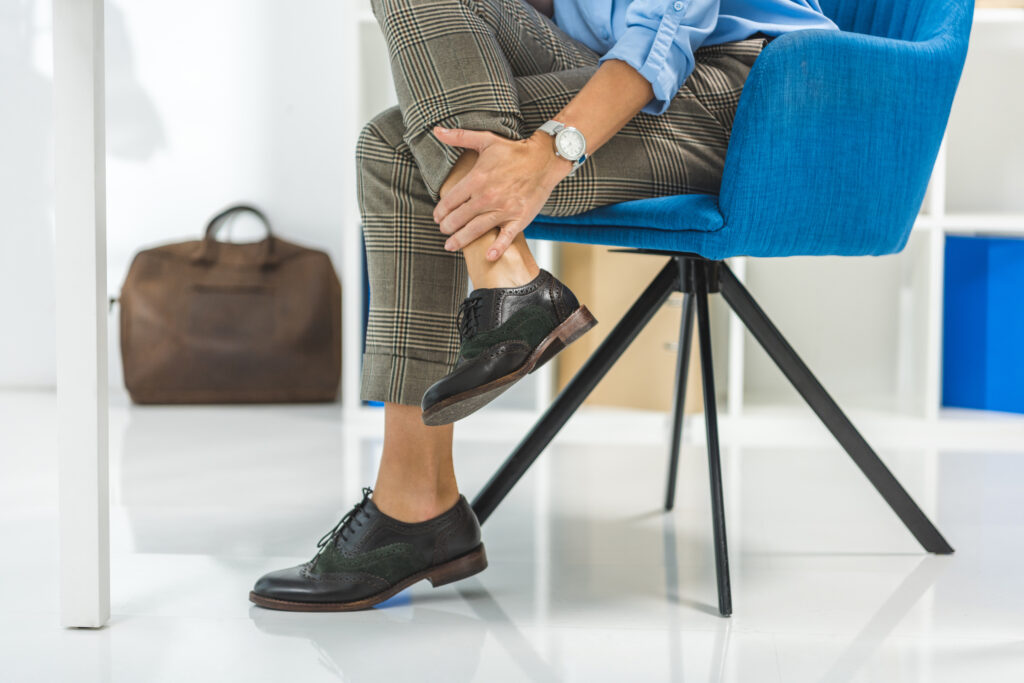 Businesswoman in office chair holding her painful lower leg, leg pain Mast Health treats for working professionals in Tampa