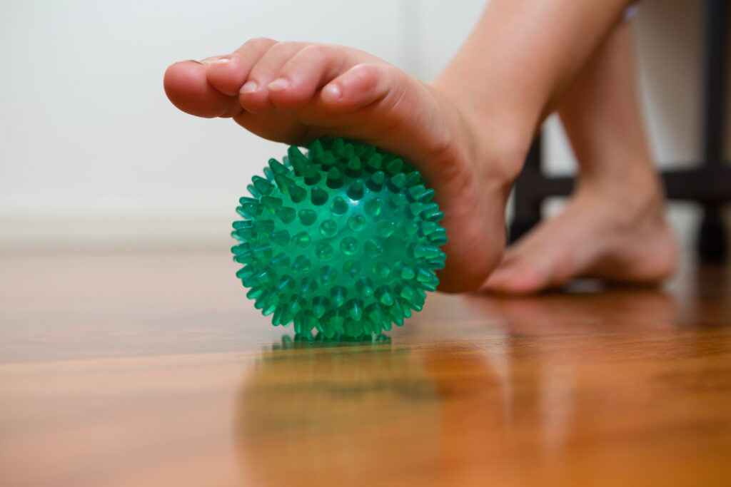 Foot rolling over a spiked massage ball indoors to release plantar fascia tightness, rehab guidance from Mast Health in Tampa, FL
