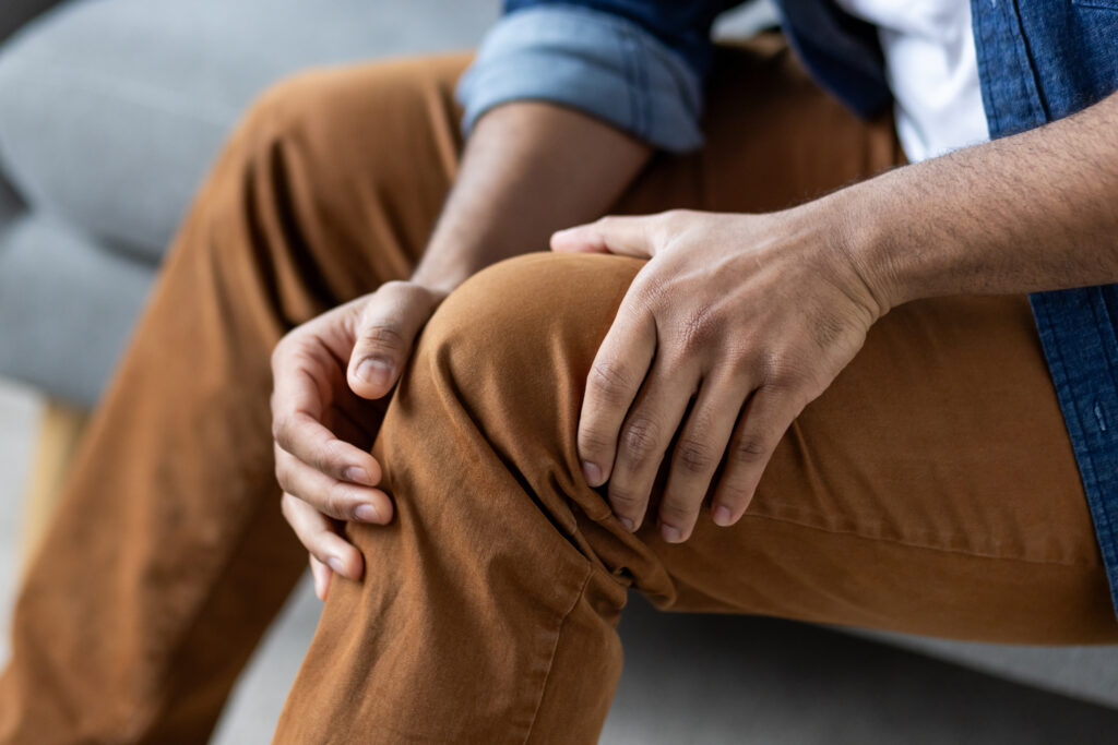 Man sitting on a sofa massaging his knee joint, knee pain Mast Health relieves for patients at home in Tampa