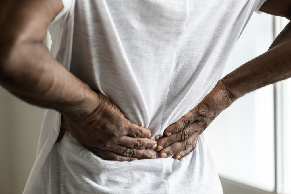 Man holding his lower back with both hands at home, sharp nerve pain treated at Mast Health in Tampa, FL