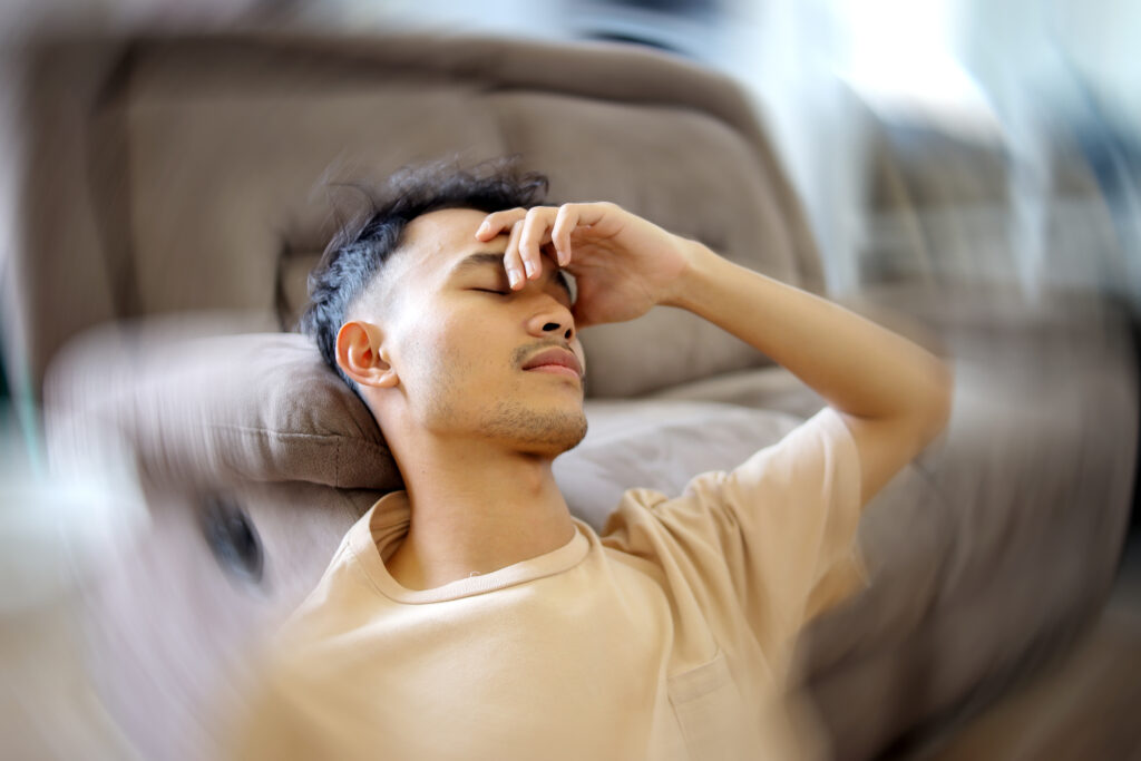 Man sitting on couch holding his head with eyes closed, experiencing dizziness and vertigo symptoms - Tampa, FL chiropractic care at Mast Health