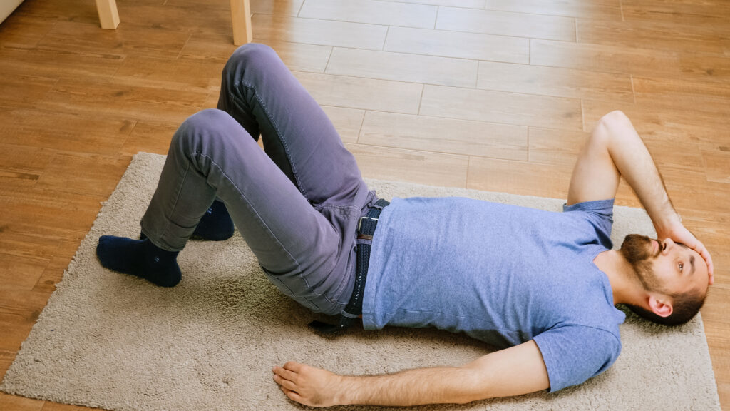 Man lying on floor holding his head, experiencing vertigo and dizziness symptoms - Tampa, FL chiropractic care at Mast Health
