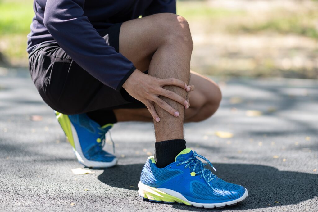 Runner kneeling to massage a painful calf muscle injury outdoors, leg pain Mast Health treats for active patients in Tampa