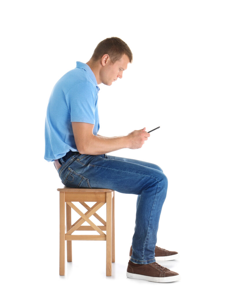 Man sitting on a stool with his head bowed forward over his phone, demonstrating tech neck posture treated at Mast Health in Tampa, FL