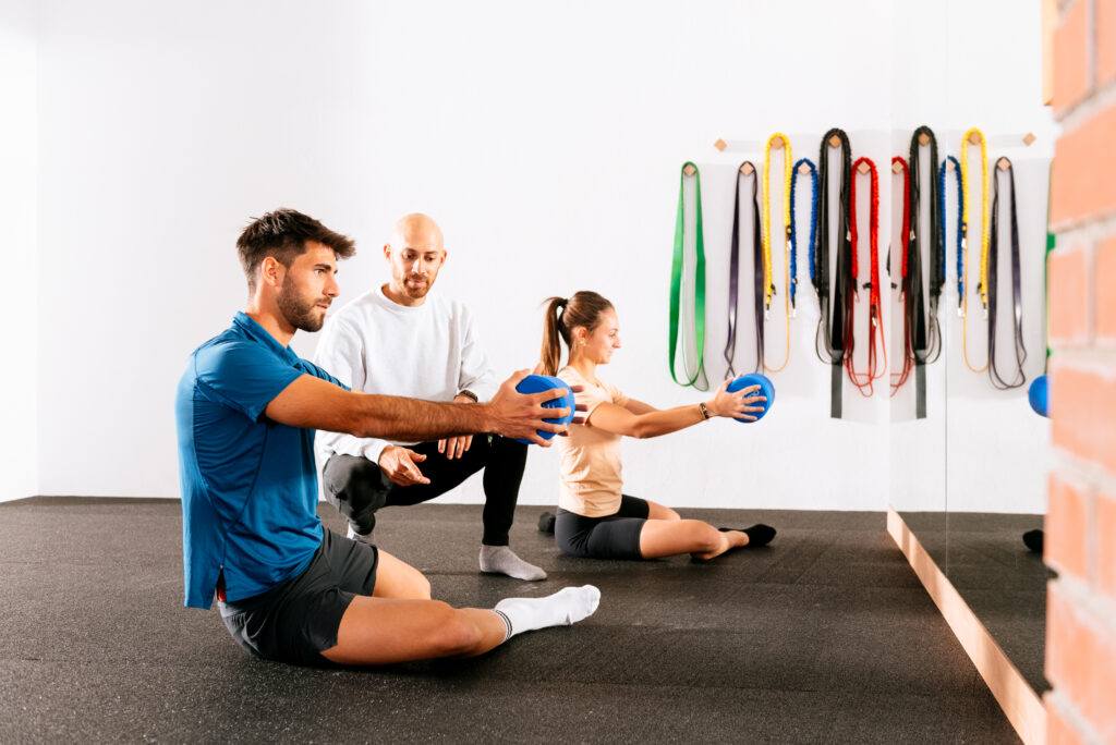 Instructor guiding a man and woman through elastic band hip mobility exercises in a gym, a technique used to relieve hip pain at Mast Health in Tampa, FL