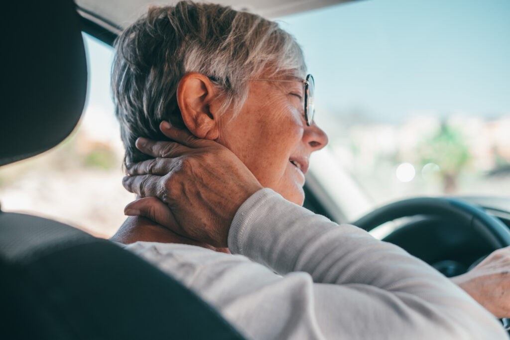 Older woman experiencing neck pain while driving after a whiplash injury