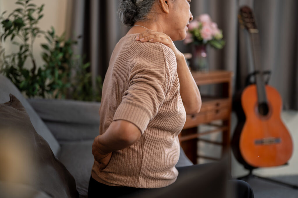 Elderly woman massaging her aching shoulder and neck while seated at home, a common sign of a pinched nerve treated at Mast Health in Tampa, FL