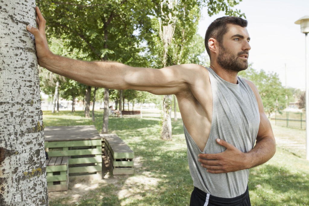 Man stretching his arm against a tree in the park to relieve shoulder pain, rotator cuff injury care available at Mast Health in Tampa, FL