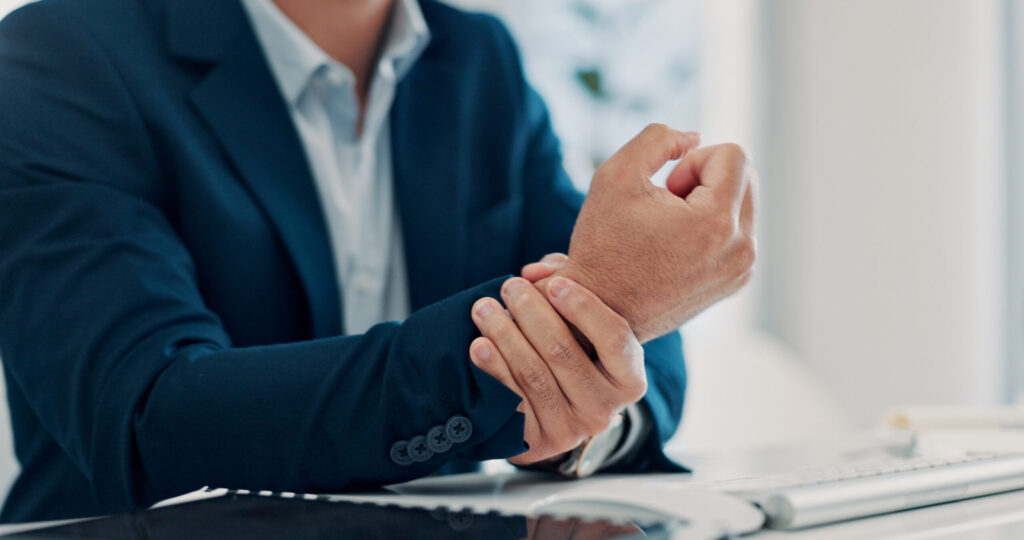 Businessman holding his wrist in discomfort at his desk, wrist pain relief available at Mast Health chiropractic clinic in Tampa, FL