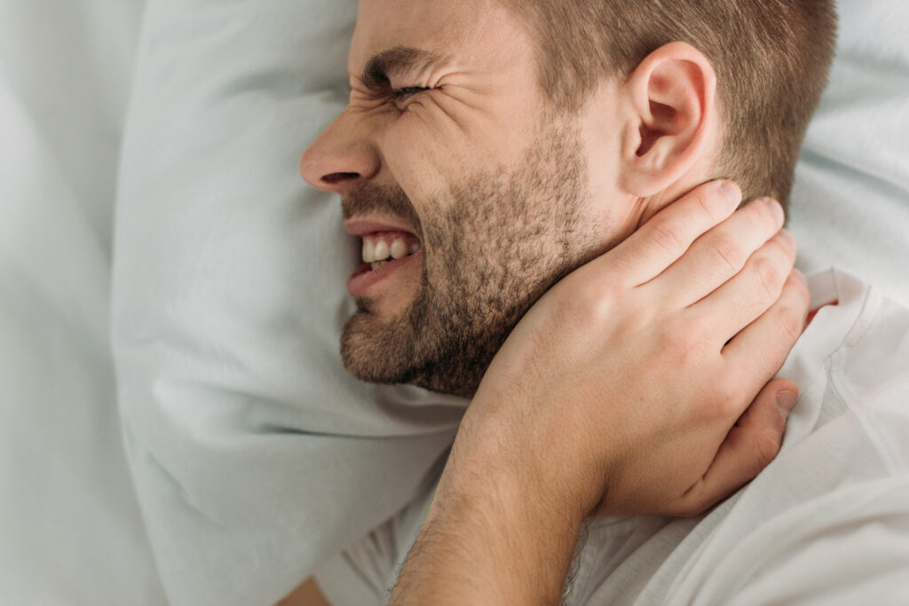 Young man wincing while touching his neck and jaw in pain, TMJ discomfort treated at Mast Health chiropractic clinic in Tampa, FL