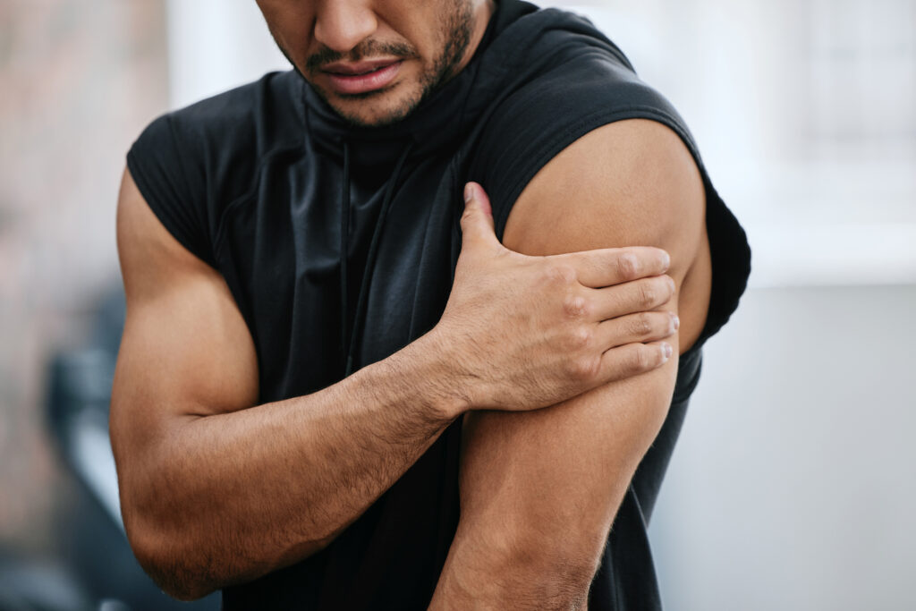 Male gym trainer rubbing his shoulder in pain, a rotator cuff strain treated at Mast Health in Tampa, FL