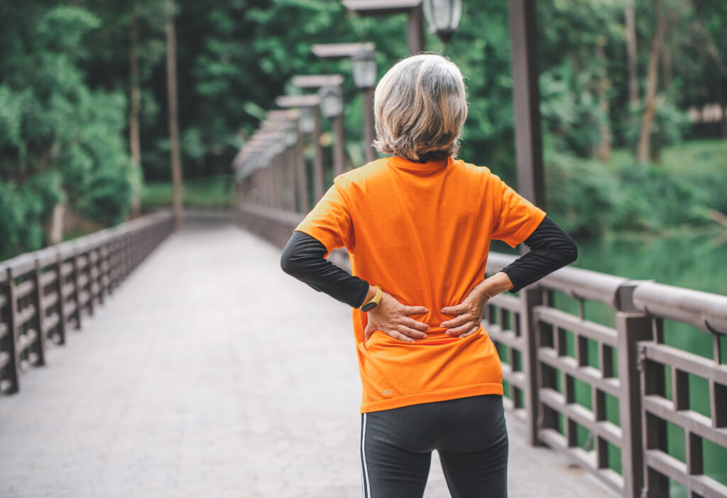 Elderly woman holding her lower back while exercising in the park, sciatica relief supported by Mast Health chiropractic care in Tampa, FL