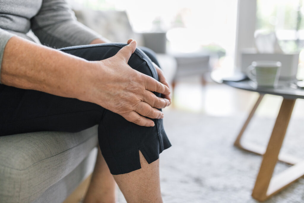 Person sitting on couch holding their sore knee, knee pain Mast Health evaluates from the hip to the foot in Tampa