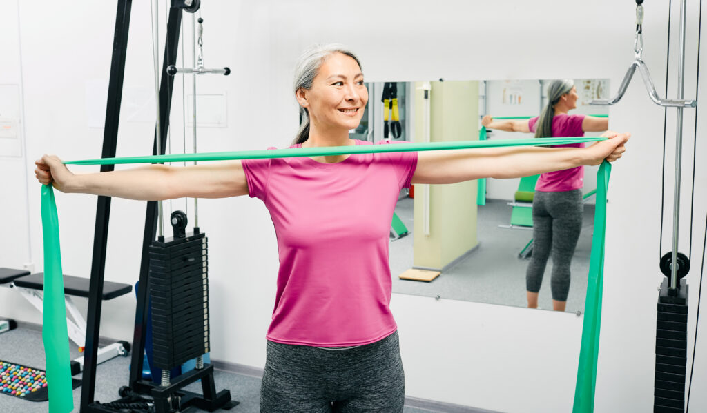 Smiling woman using a resistance band for shoulder rehab exercises at a Mast Health rotator cuff recovery session in Tampa, FL