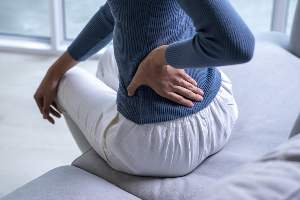 Woman sitting on a couch holding her lower back and hip in pain, a condition treated at Mast Health in Tampa, FL
