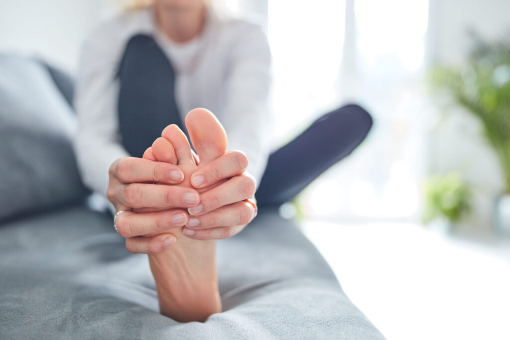 Woman massaging her own foot while sitting on the couch at home to relieve foot pain, a technique recommended at Mast Health in Tampa, FL