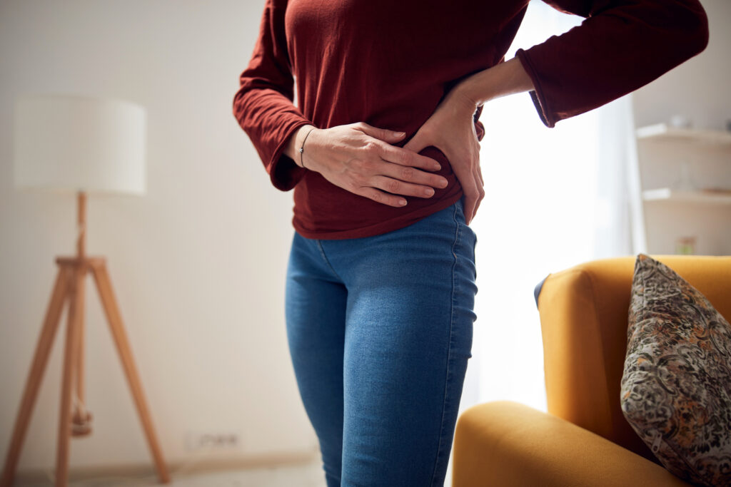 Woman standing at home holding her hip in discomfort, a common symptom of hip pain treated at Mast Health in Tampa, FL