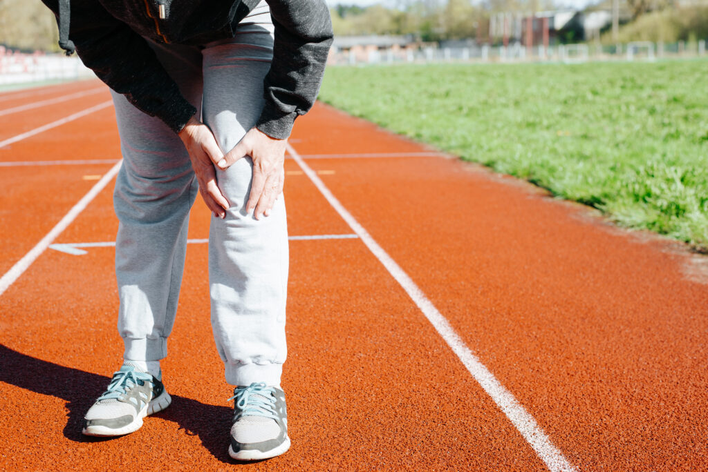 Female runner on a track holding her knee in pain, a sign of an overuse injury treated at Mast Health in Tampa, FL