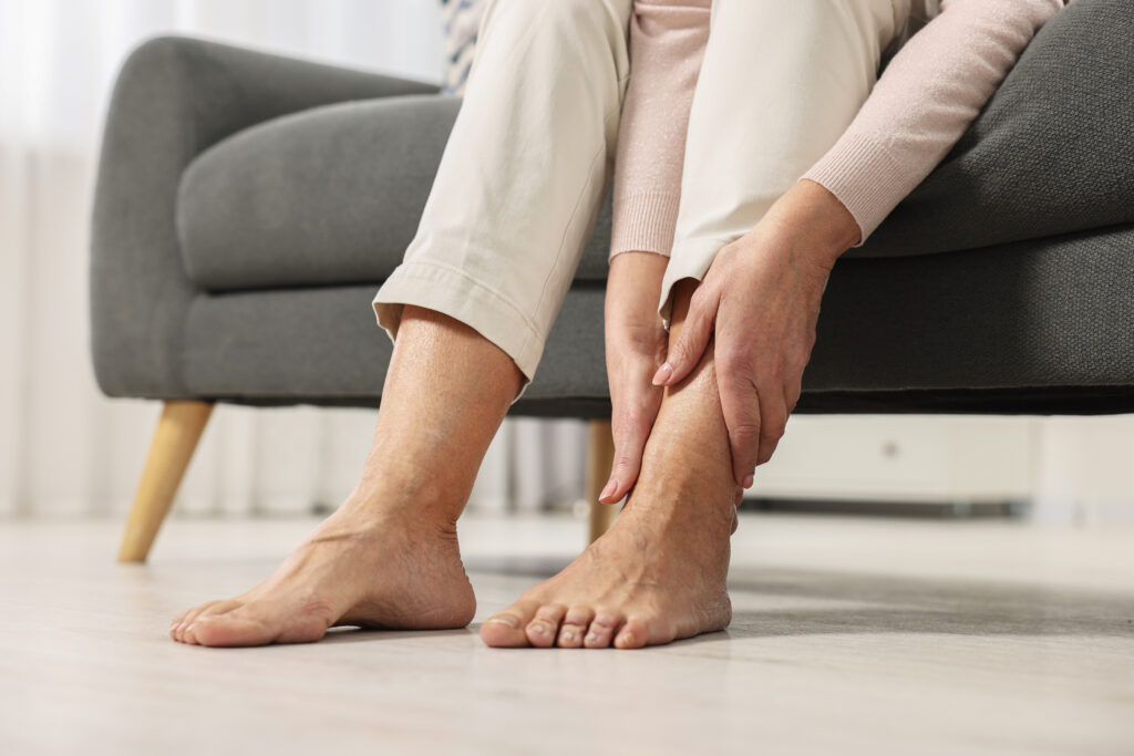Woman seated on a couch massaging pain in her lower leg and ankle, a symptom Mast Health evaluates for neuropathy in Tampa