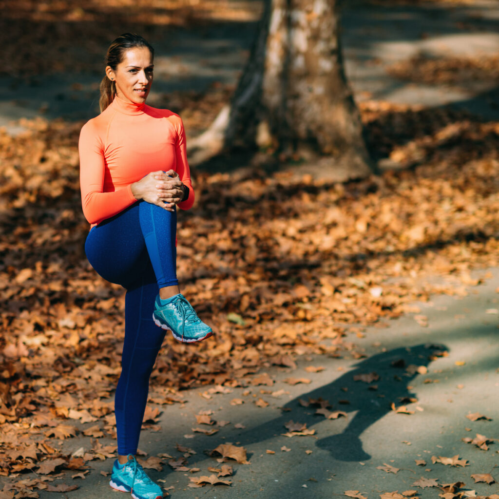 Woman stretching her leg outdoors in a park after a run, knee pain Mast Health helps active Tampa patients prevent