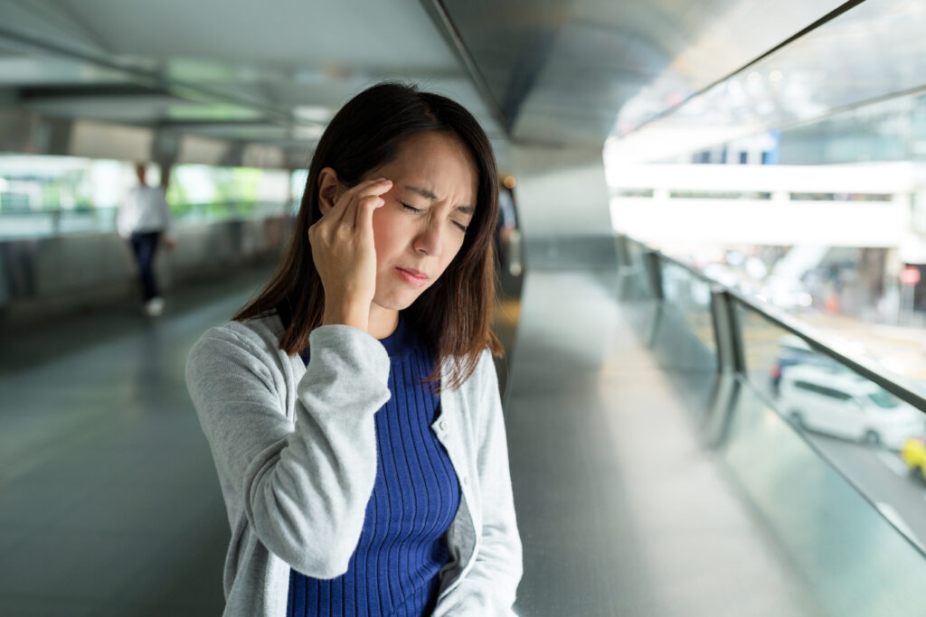 Woman standing in an elevated walkway holding her head in pain, a vertigo symptom treated at Mast Health in Tampa, FL