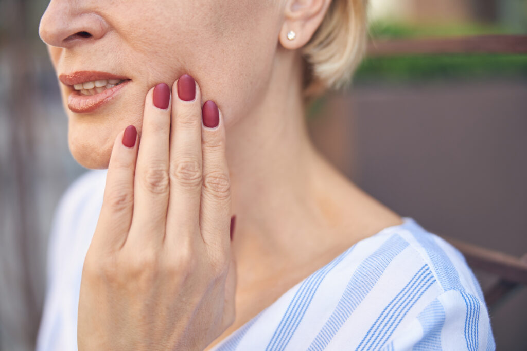Woman touching her cheek in acute jaw and dental pain, TMJ relief offered at Mast Health chiropractic clinic in Tampa, FL