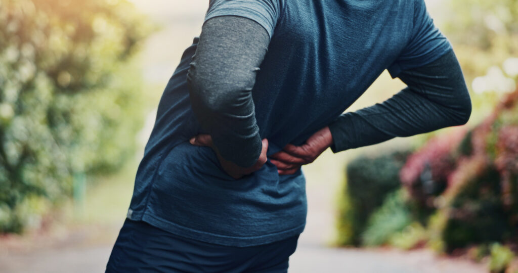 Man holding lower back in pain during outdoor workout, seeking sciatica relief through chiropractic care at Mast Health in Tampa, FL