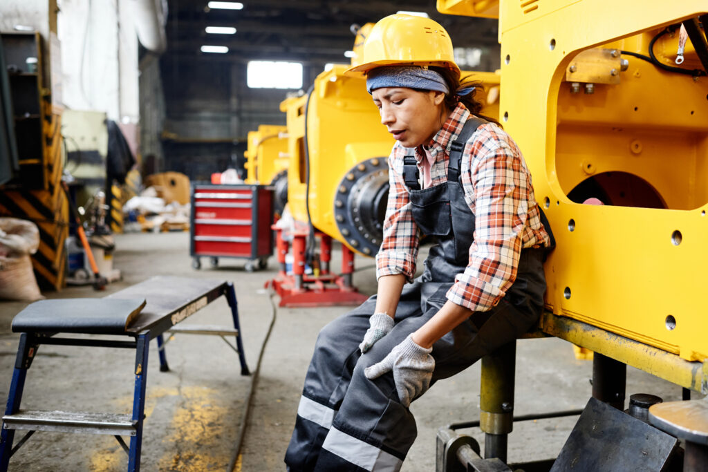 Young female factory worker sitting and holding her knee in pain while working, a sign of an overuse injury treated at Mast Health in Tampa, FL